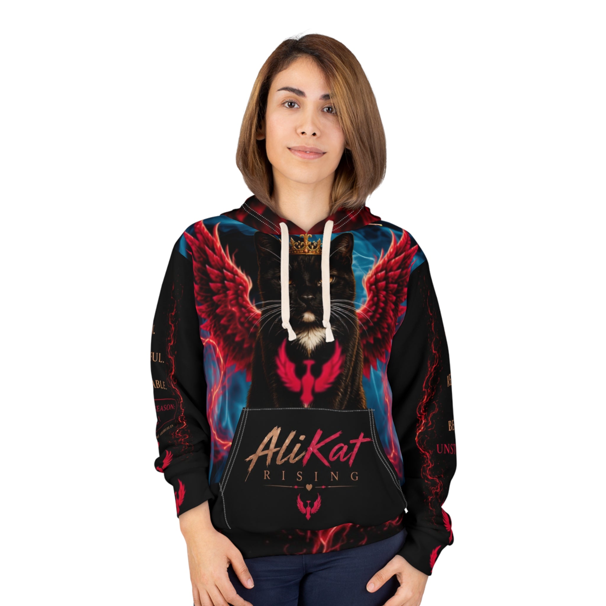 A woman with straight brown hair is seen wearing the AliKat Rising Phoenix Vol. 1 Premium Motivational Hoodie, which features a winged black cat with a crown and the words "AliKat Rising" on the front. She stands facing forward, smiling slightly. For your ideal fit, please refer to the size chart; this hoodie is available in XS, S, M, L, XL, and 2XL from AliKat Rising.