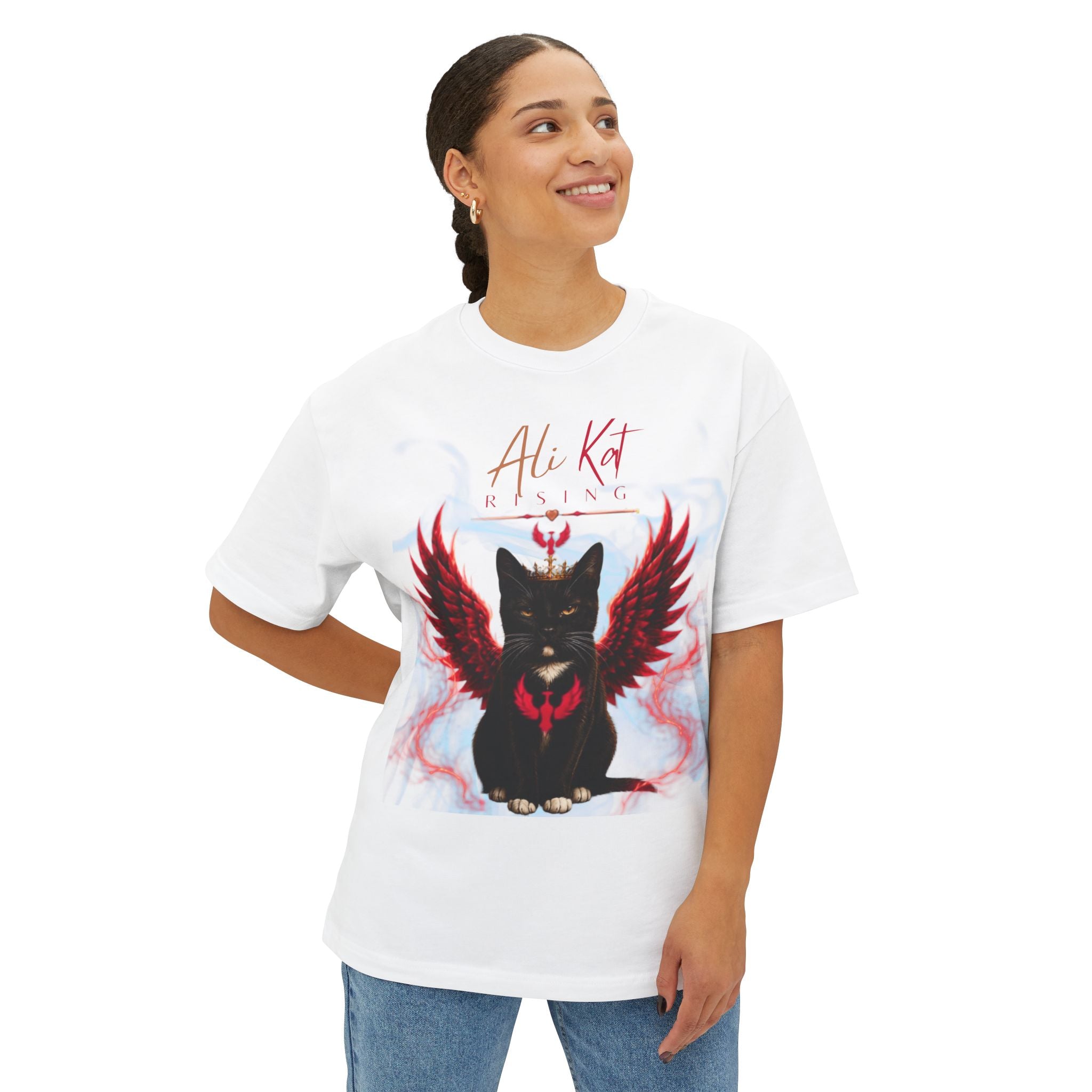 A smiling person wears the AliKat Rising Phoenix Season: Vol. 1 Signature Oversized Tee—a premium, heavyweight cotton unisex t-shirt with an oversized fit. The shirt features a black cat with red wings and a crown, along with the AliKat Rising text, as part of the Phoenix Season Signature collection.