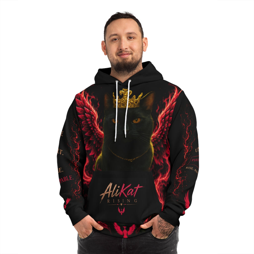 A man smiles and stands with his hands clasped in front of him, wearing the Phoenix Wings Hoodie — AliKat Flame Graphic Pullover by AliKat Rising. The black hoodie showcases a striking graphic of a black cat adorned with a gold crown and red wings, along with the signature AliKat Rising text. Available in sizes S, M, L, XL, and 2XL—with detailed length and width measurements for the perfect fit.