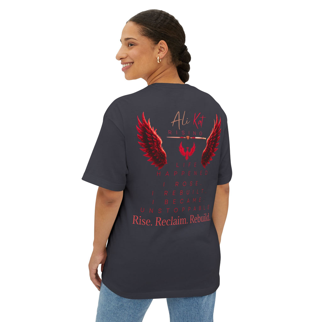 A smiling woman wears the AliKat Rising Phoenix Season: Vol. 1 Signature Oversized Tee, crafted from premium heavyweight cotton. This unisex t-shirt showcases bold red wing graphics and inspiring text on the back: Life happened. I rose. I rebuilt. I became unstoppable. Rise. Reclaim. Rebuild.—a powerful embodiment of resilience and the unstoppable spirit of Phoenix Season.